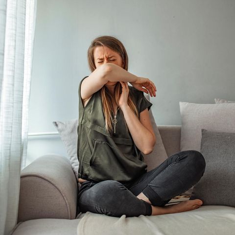 Symptome von Corona, Erkältung, Grippe: Eine Frau sitzt auf einem Sofa und hustet