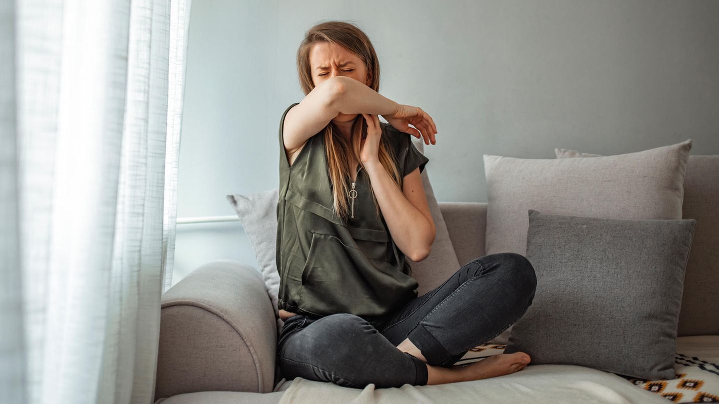 Symptome von Corona, Erkältung, Grippe: Eine Frau sitzt auf einem Sofa und hustet