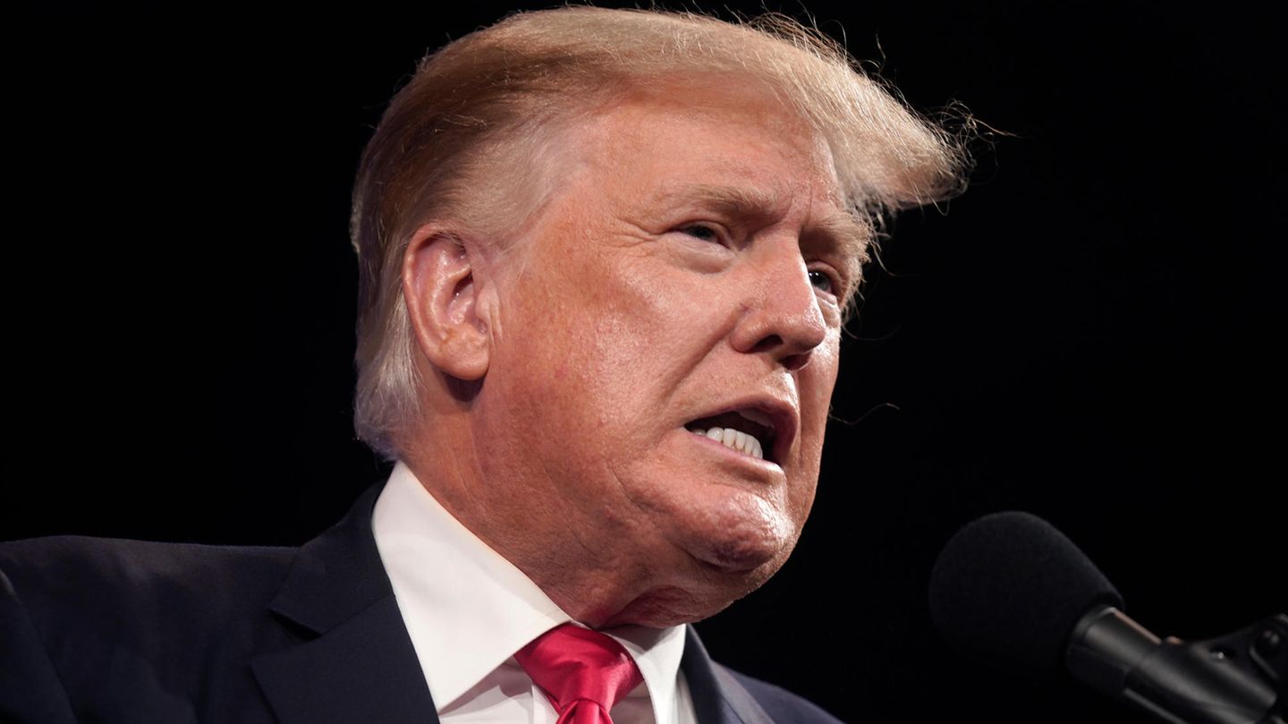 Donald Trump mit verzerrtem Mund vor einem Mikrofon