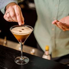 Espresso Martini: Ein Barkeeper garniert den vollendeten Espresso Martini mit drei Kaffeebohnen.
