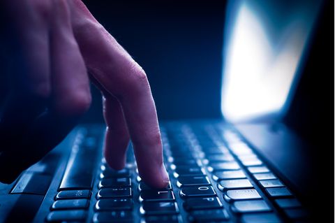 Finger tippt auf einer Tastatur, dunkle Umgebung und Gegegnlicht