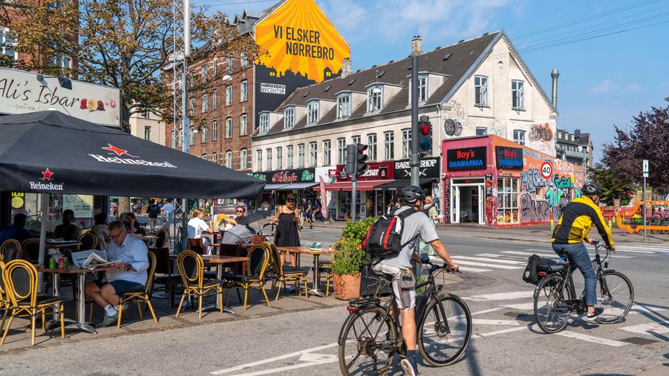 Fahrradfahrer halten an Ampel, im Hintergrund bunte Cafés. Fahrradfahrer halten an Ampel, im Hintergrund bunte Cafés.