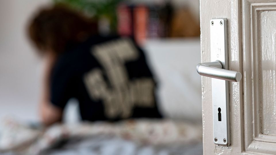 50 Prozent von der Freiheit gestresst - "Höhlen-Syndrom" hemmt junge Menschen nach Pandemie Junge Frau sitzt mit Rücken zur Kamera und gesenktem Kopf auf dem Bett