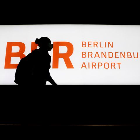 Passagierin läuft an einem beleucteten Schild BER Berlin Brandenburg Airport vorbei