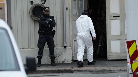 Techniker der Polizei geht nach einer Gewalttat mit fünf Toten und zwei Verletzten in ein Gebäude, vor dem ein Polizist Wache steht