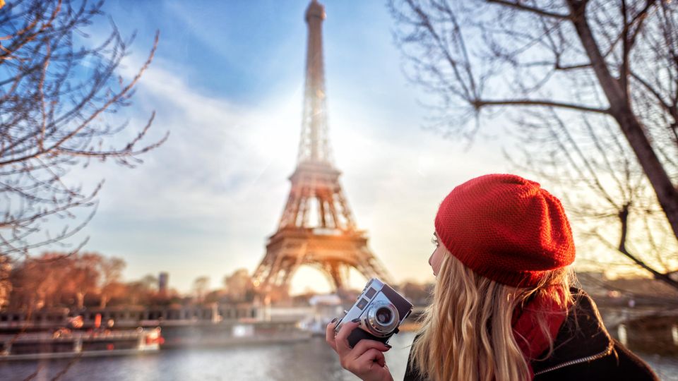 Junge Frau sitzt mit einer Kamera in der Hand vor dem Eiffelturm in Paris