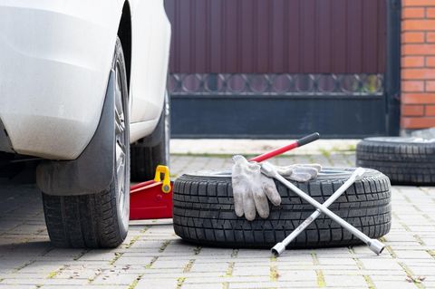 Reifenwechsel selber machen: Radkreuz und Räder liegen neben einem PKW