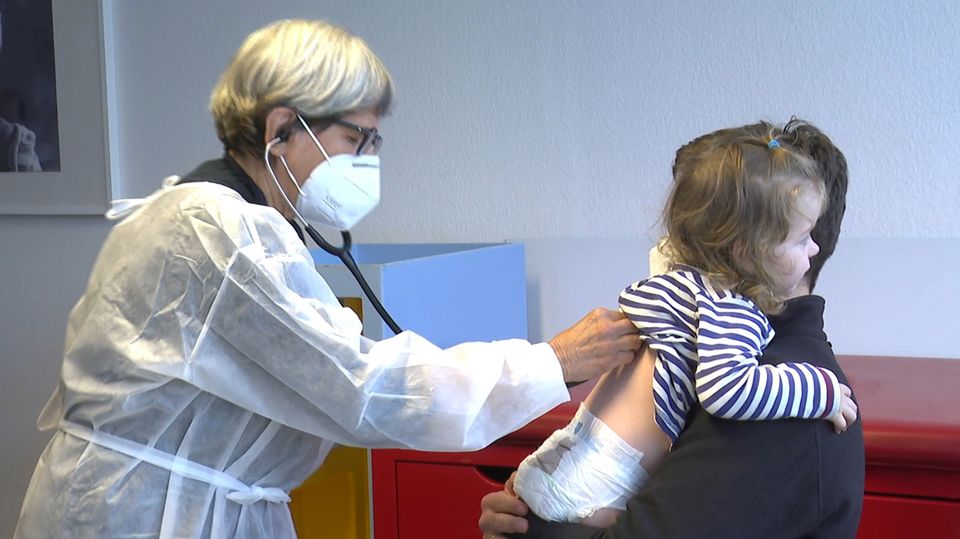 Eine Ärztin horcht ein Kind auf dem Arm ihres Vaters ab.