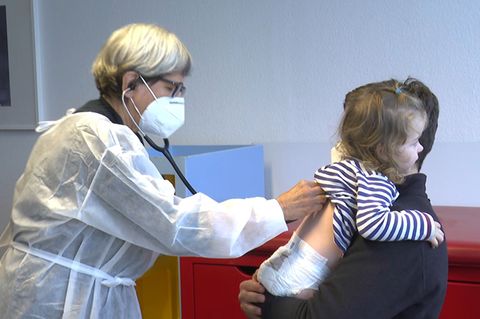 Eine Ärztin horcht ein Kind auf dem Arm ihres Vaters ab.