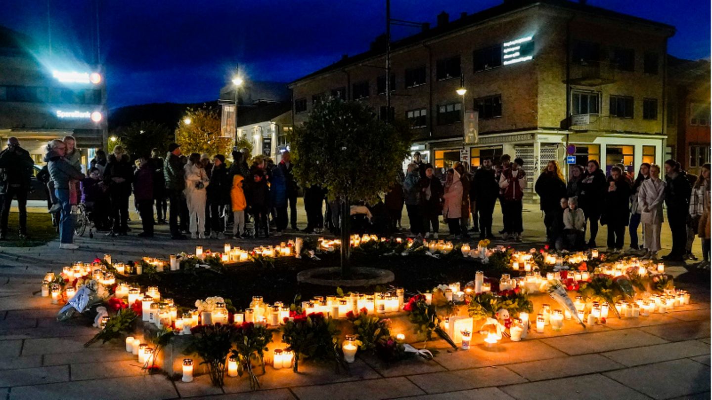Personen stehen vor Blumen und Kerzen, die in Gedenken an die Opfer niedergelegt wurden
