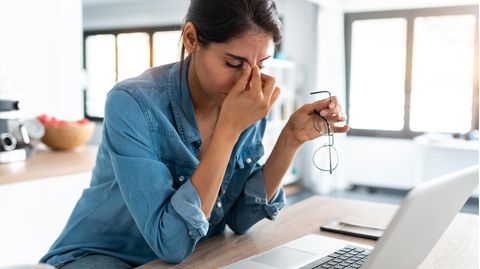 Stresssymptome: Eine Frau hat Stress auf der Arbeit und fasst sich an den Kopf