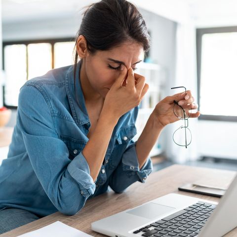 Stresssymptome: Eine Frau hat Stress auf der Arbeit und fasst sich an den Kopf