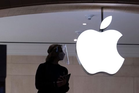 Eine Mitarbeiterin steht vor einer Glaswand mit dem leuchtenden Apple-Logo.