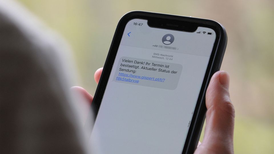 Eine Person hält ein Handy in der Hand, eine SMS zeigt einen Phishing-Link.