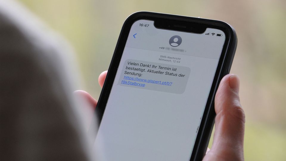 Someone is holding a cell phone and a text message shows a phishing link.