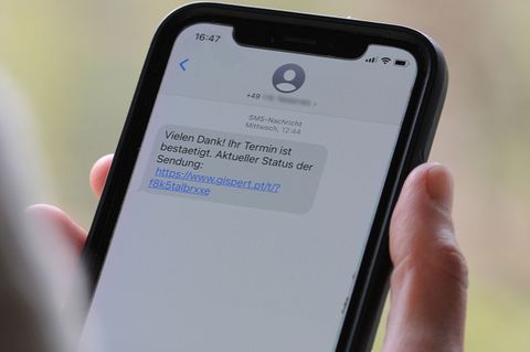 Eine Person hält ein Handy in der Hand, eine SMS zeigt einen Phishing-Link.