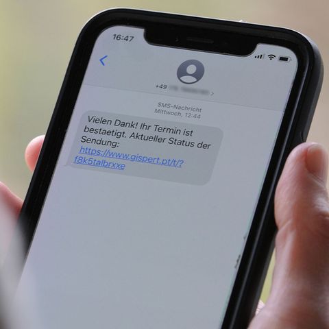 Eine Person hält ein Handy in der Hand, eine SMS zeigt einen Phishing-Link.