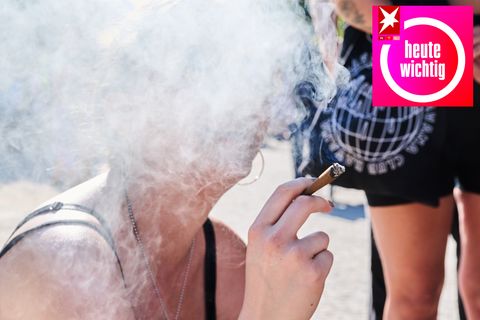 Das Gesicht einer jungen, weißen Frau verschwindet in einer Rauchwolke, während die Frau mit rechts einen Joint hält