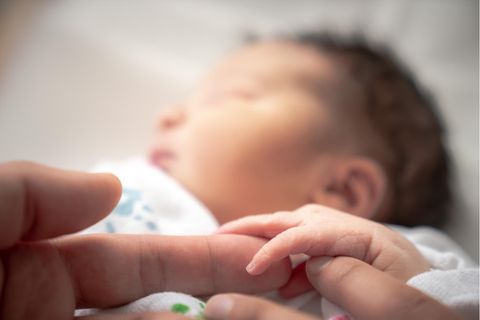 Ein Baby hält schlafend die Hand eines Erwachsenen.