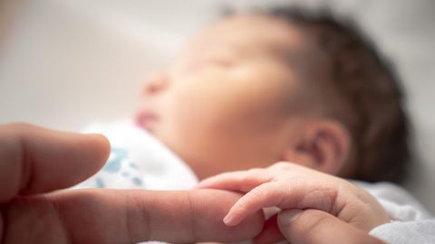 Ein Baby hält schlafend die Hand eines Erwachsenen.