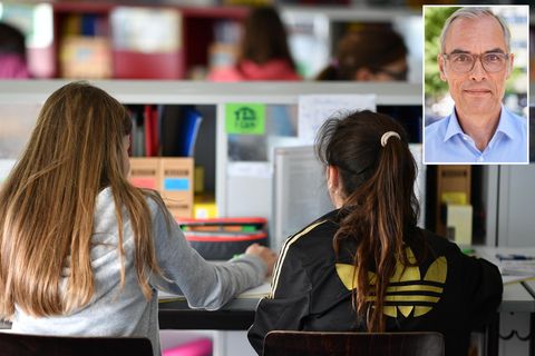 Von hinten sind zwei Schülerinnen mit langen Haaren zu sehen, die gemeinsam in einem Klassenraum sitzen