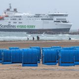 Spaziergänger sind im Regen am Ostseestrand unterwegs - im Hintergrund ein Fährschiff