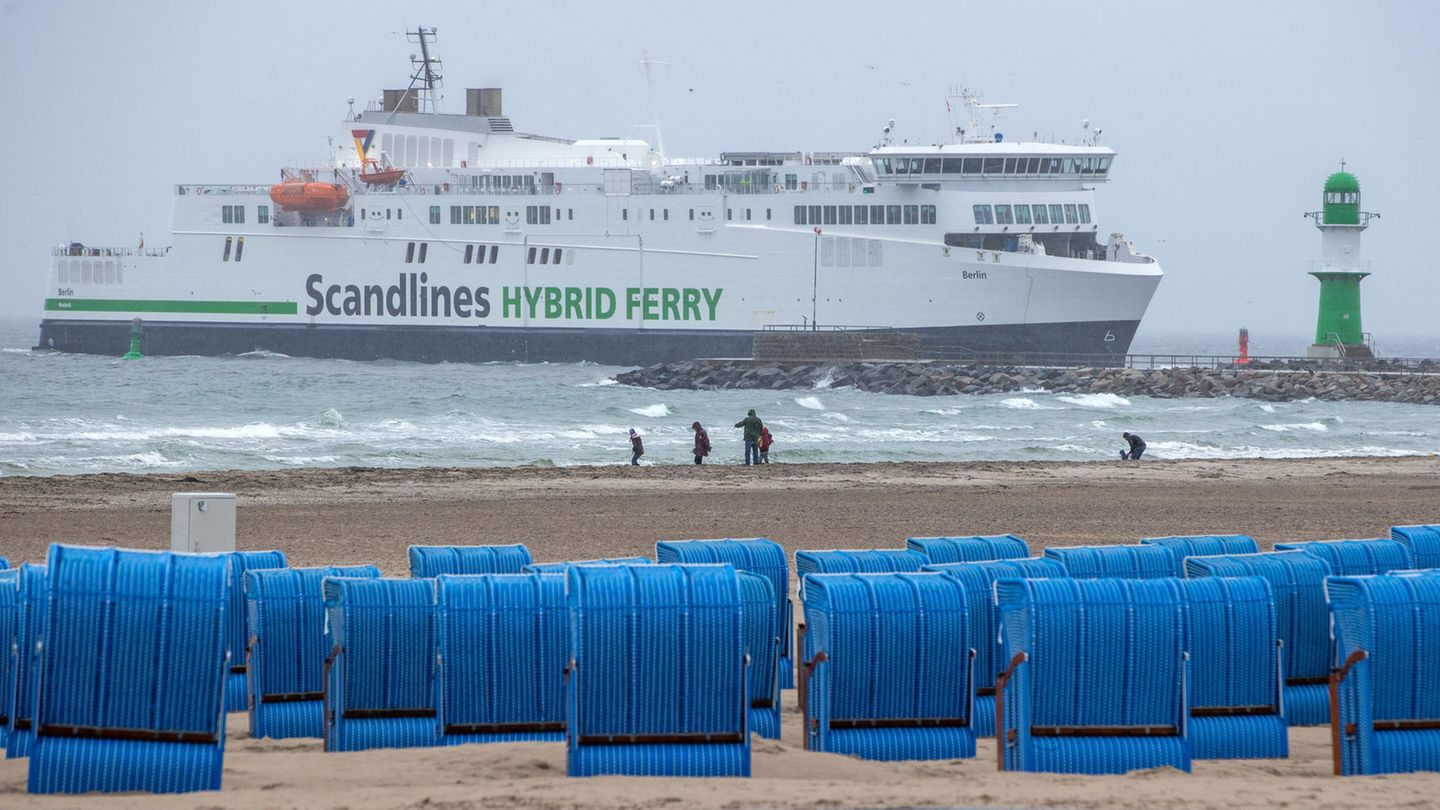 Spaziergänger sind im Regen am Ostseestrand unterwegs - im Hintergrund ein Fährschiff