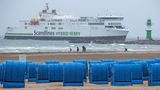 Spaziergänger sind im Regen am Ostseestrand unterwegs - im Hintergrund ein Fährschiff