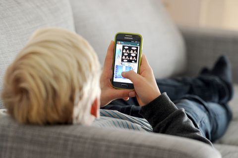 Ein Kind liegt mit einem Smartphone auf einem Sofa