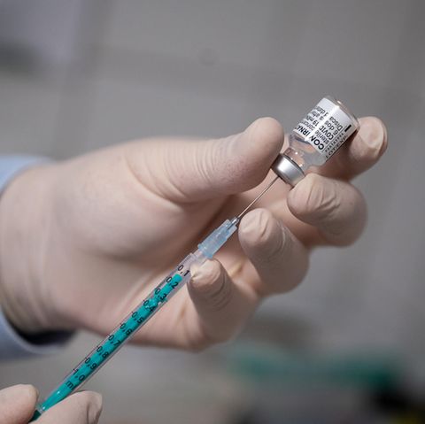 Eine linke Hand in weißem Gummihandschuh hält eine Ampulle, während eine rechte eine Spritze daraus aufzieht