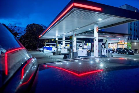 In der Dämmerung spiegelt sich das rote Licht eines Tankstellendaches im Lack eines Autos