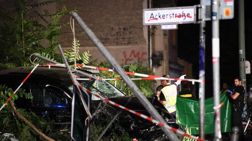 An einem zerstörten Auto halten Polizisten ein Plane An einem zerstörten Auto halten Polizisten ein Plane