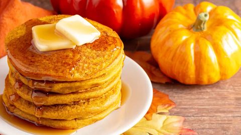 Pancakes auf einem Teller, dekoriert mit Kürbissen und Herbstlaub.