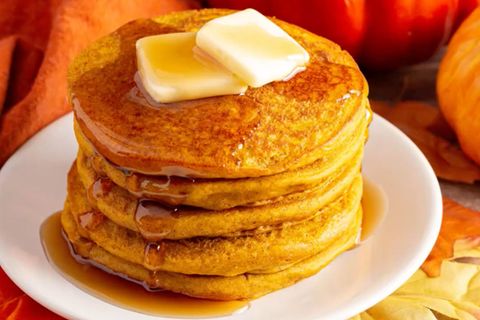 Pancakes auf einem Teller, dekoriert mit Kürbissen und Herbstlaub.