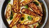 Gegrillte Zucchini mit Joghurtsauce und Safranbutter      Zutaten:  30 g Butter, ¼ TL Safranfäden, grob zerstoßen, 4 kleine Zucchini, vom Stielansatz befreit und längs halbiert (600 g), 2½ EL Olivenöl, 1 TL Speisestärke, 300 g griechischer Joghurt, 2 Knoblauchzehen, zerdrückt, ½ TL getrocknete Minze, ¾ TL Korianderkörner, geröstet und im Mörser grob zerstoßen, 1½ EL Minzeblätter, ½ Zitrone, Salz und schwarzer Pfeffer      Zubereitung:  1. Den Backofengrill vorheizen.  2. Die Butter mit dem Safran in einen kleinen Topf geben. Bei mittlerer Hitze zerlassen, dann vom Herd nehmen, beiseitestellen und ziehen lassen.  3. Die Zucchini auf ein mit Back- papier ausgelegtes Blech geben. Mit 2 EL Öl, . TL Salz und 1 kräftigen Prise Pfeffer durchheben. Anschließend mit der Schnittfläche nach oben 15–20 Minuten grillen, bis sie gut gebräunt und weich sind.  4. In den letzten 10 Minuten der Garzeit für die Sauce die Speisestärke in einer großen Schüssel mit 3 EL Wasser glatt rühren, dann Joghurt, Knoblauch, getrocknete Minze, den restlichen ½ EL Öl sowie ½ TL Salz dazugeben und alles verquirlen. Die Mischung in eine große antihaftbeschichtete Pfanne gießen und bei mittlerer Temperatur 10 Minuten erhitzen. Unablässig rühren, bis die Sauce warm ist und leicht eindickt. Sie darf nicht aufkochen, sonst gerinnt sie.  5. Die warme Joghurtsauce in eine Schale gießen, die Zucchini mit der Schnittfläche nach oben darauf anrichten. Das Ganze mit der Safranbutter beträufeln, dann mit Koriander und Minzeblättern bestreuen. Die Zitronenhälfte darüber auspressen und das Gericht sofort servieren.