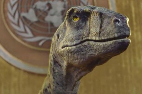 Ein Dinosaurier steht vor dem Rednerpult des UNO-Parlamentes.