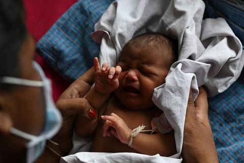 Eine indische Mutter hält ihr in ein weißes Tuch gewickeltes Neugeborenes auf dem Schoß