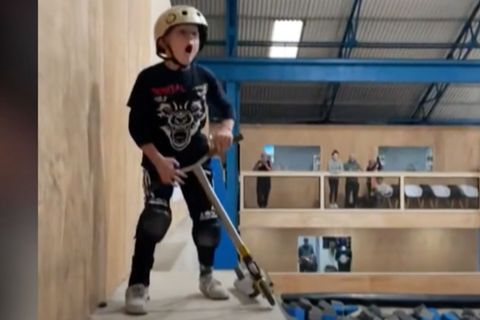 Ein kleiner Junge steht mit offenem Mund und seinem Scooter in den Händen auf einer Halfpipe.