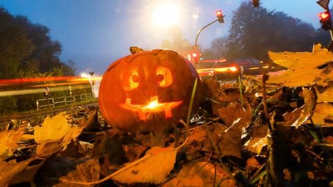 Ein von innen beleuchteter, ausgehöhlter, zu einem Gesicht geschnitzter Kürbis steht an Halloween an einer Straße