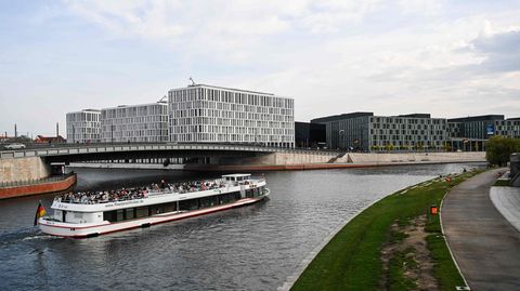 Ein weißes Ausflugsschiff mit roten Streifen und offenem Oberdeck fährt auf der Spree durchs Regierungsviertel in Berlin