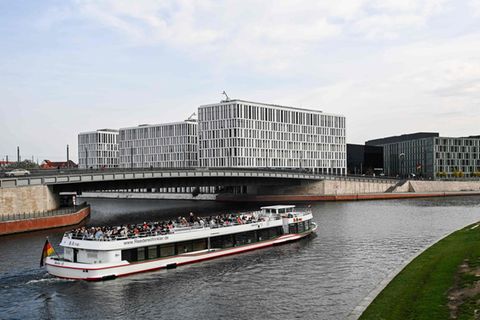 Ein weißes Ausflugsschiff mit roten Streifen und offenem Oberdeck fährt auf der Spree durchs Regierungsviertel in Berlin
