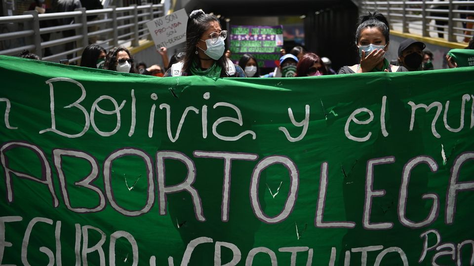 Zwei Frauen halten ein menschengroßes Protest-Banner vor sich, im Hintergrund weitere Demonstranten