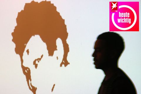 Die Konturen eines Mannes gehen auf ein an die Wand projiziertes Konterfei von Oury Jalloh zu