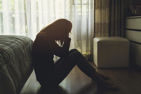 Frau sitzt in dunklem Zimmer auf dem Boden und ist traurig.
