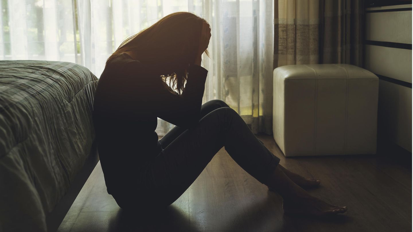 Frau sitzt in dunklem Zimmer auf dem Boden und ist traurig.