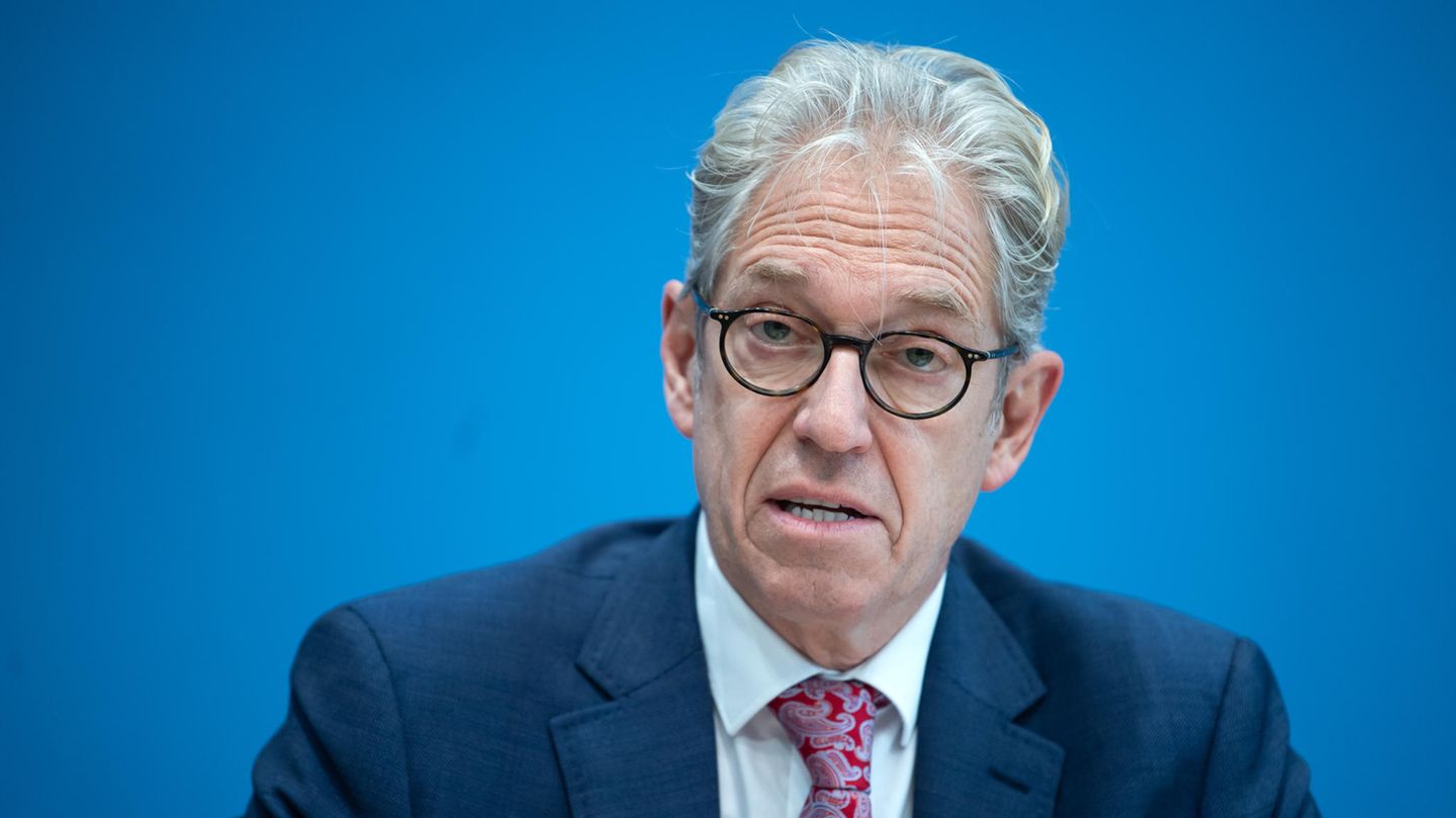 Ein älterer weißer Mann mit grau-weißem, gelocktem Haar und dunklem Brillengestell spricht im Anzug auf einem Podium