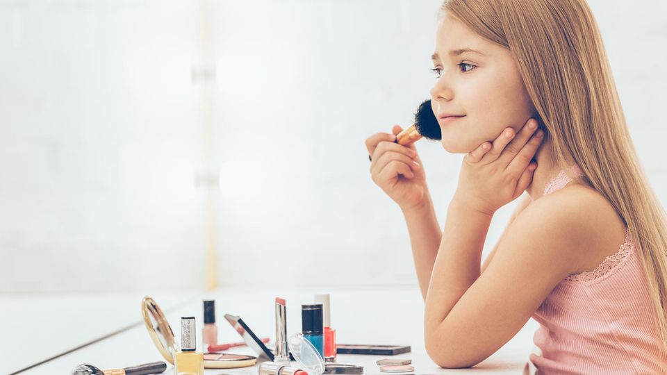 Ein junges Mädchen sitzt vor einem Spiegel und schminkt sich.