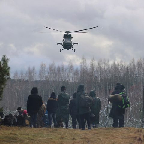 Ein polnischer Militärhubschrauber fliegt über eine Gruppe Migranten