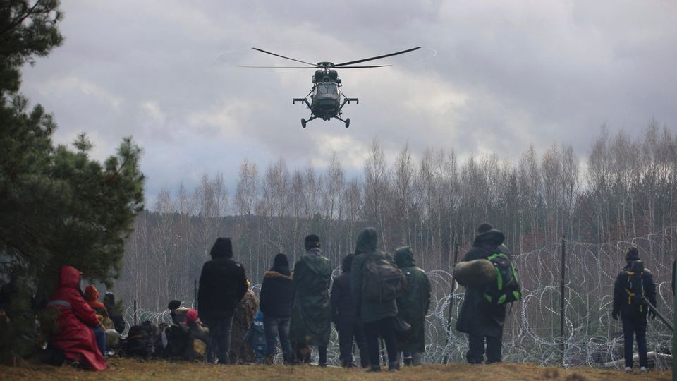 Ein polnischer Militärhubschrauber fliegt über eine Gruppe Migranten