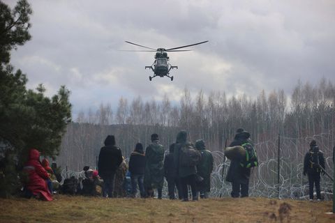 Ein polnischer Militärhubschrauber fliegt über eine Gruppe Migranten